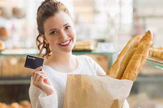 [Translate to English:] Frau in Bäckerei mit Baguette und Kundenkarte in der Hand